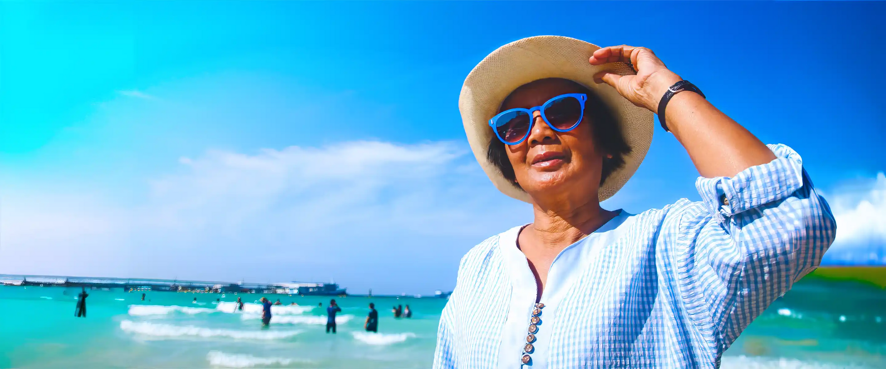 Elderly woman on sunny beach in sunglasses and hat