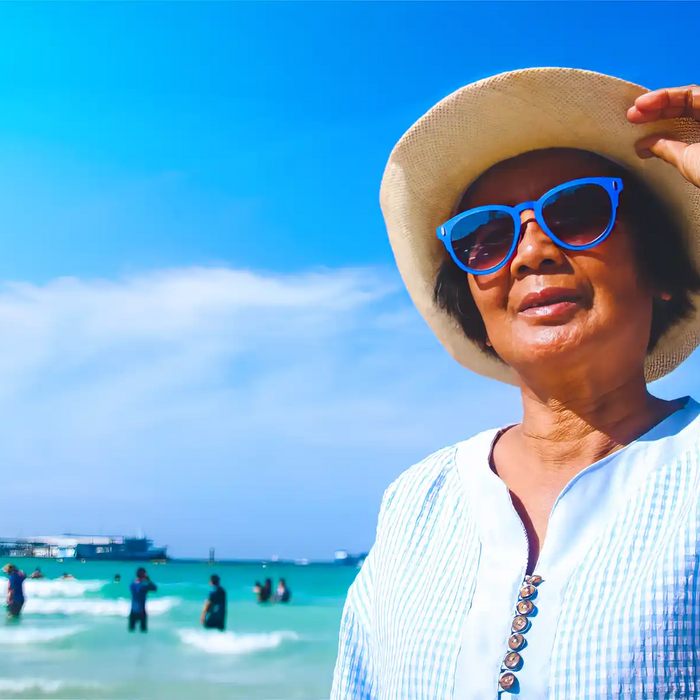 Elderly woman on sunny beach in sunglasses and hat