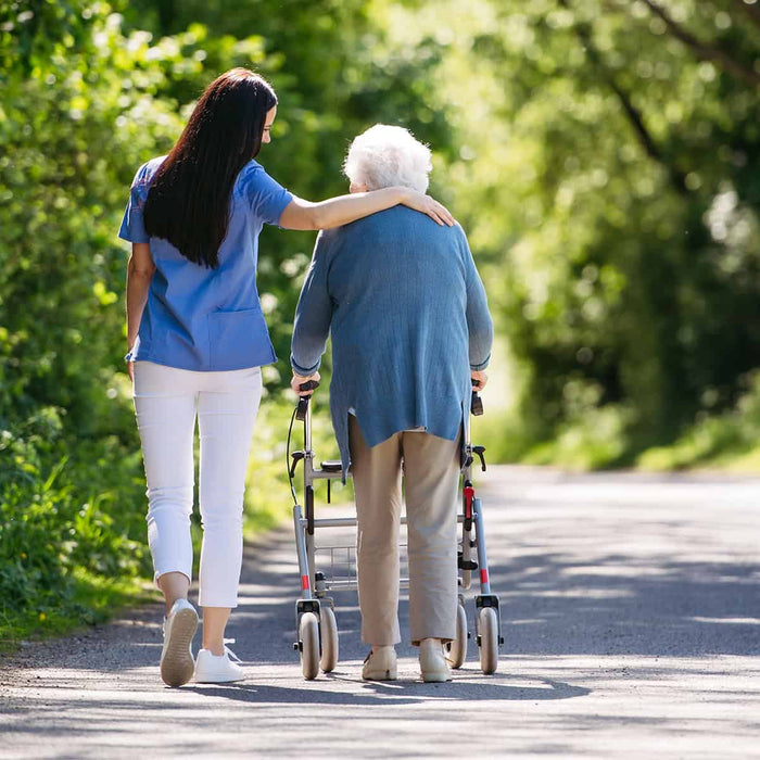 Female caregiver and senior woman with walker on walk in nature
